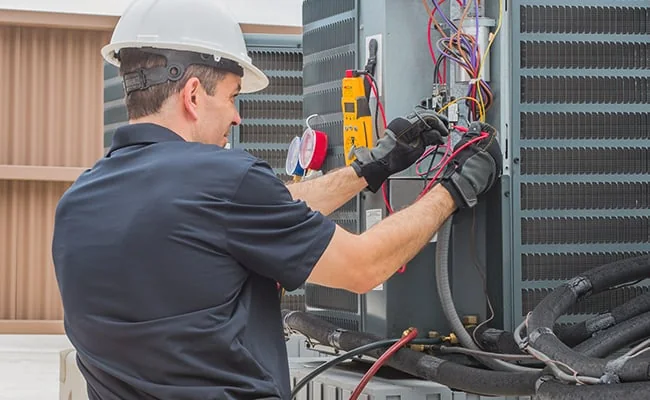 Technician testing the electrical connections on an outdoor air conditioner
